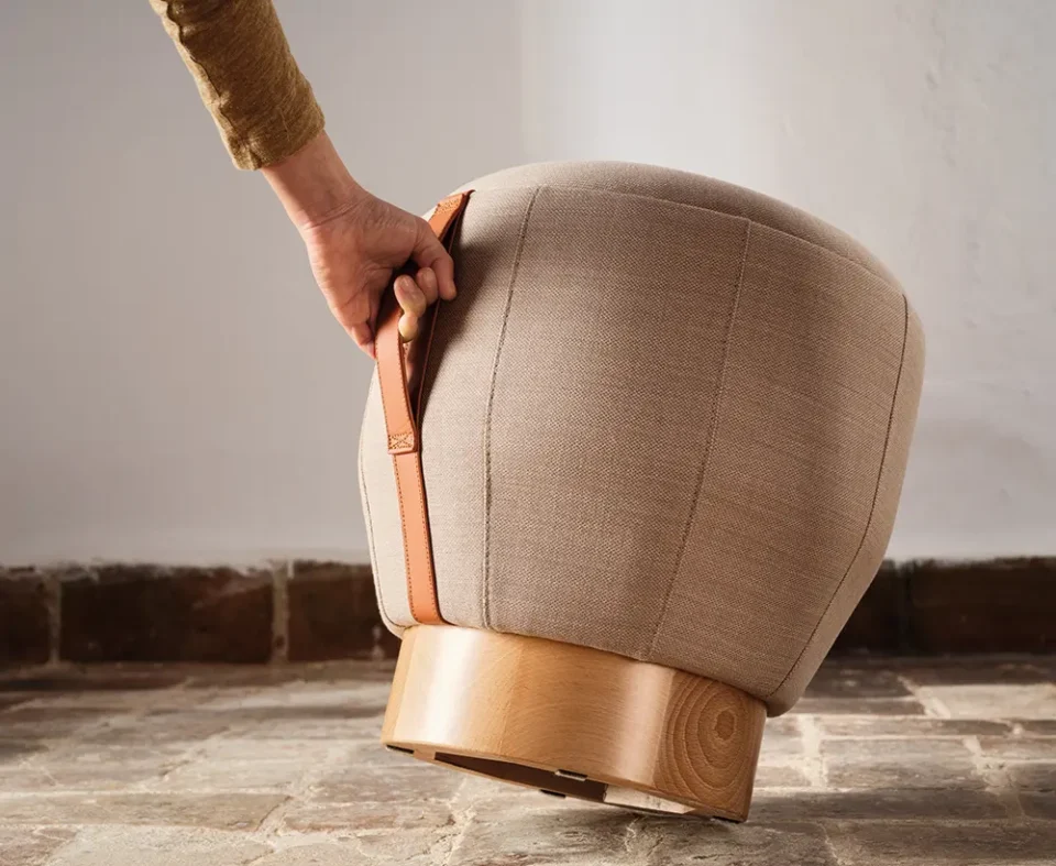 Pouf haut de gamme beige avec poignée en cuir en tissus pour entreprises, bar et restaurant en extérieur différentes tailles sur une terrasse vue de près avec une main